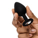 A hand holds the Fifty Shades of Grey Come to Bed Kit’s small black silicone butt plug with a flared base and clear gem, adding elegance—perfect for couples’ sensual exploration. The background is white.