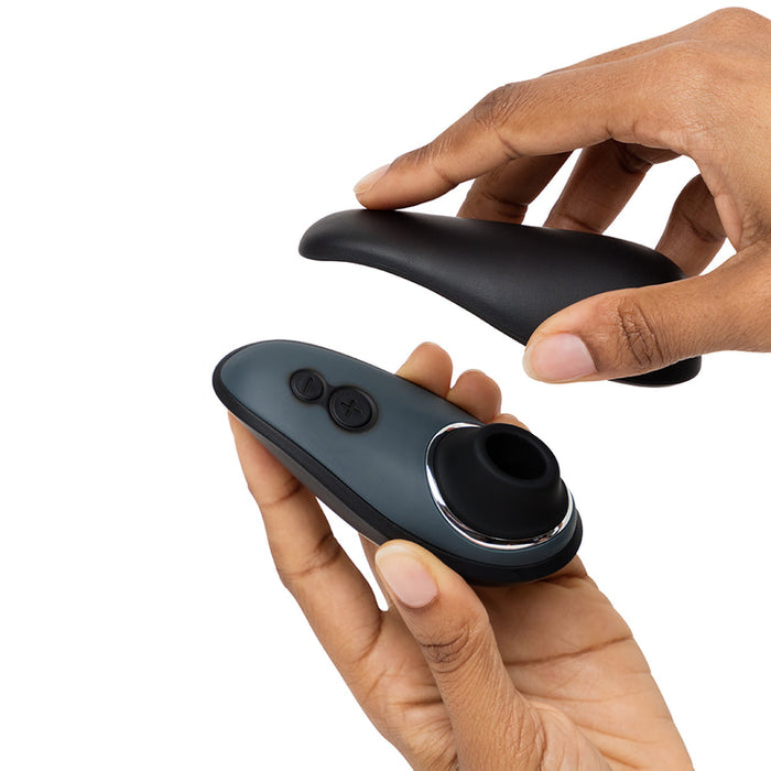 Two hands hold and open a sleek, black and gray device with buttons and a circular opening—part of the Fifty Shades of Grey Desire Blooms Kit—against a white background, suggesting a luxury couples kit.