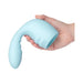 A hand holds the Flexi Posable Silicone Wand Attachment—a light blue, curved silicone accessory with a bulbous, ribbed end designed for internal and external stimulation when used with a wand massager.