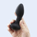 A hand holds the Frenzy Pressure Sensing App-Controlled Butt Plug, a black, ribbed toy with a flared base, against a light grey background.