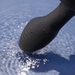 A close-up of the Frenzy Pressure Sensing App-Controlled Butt Plug's black applicator touches water, creating gentle ripples and small splashes.