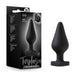 A black Fuck Me Silicone Heart Butt Plug from Blush, featuring a tapered shape and heart-shaped base, is displayed alongside its predominantly black packaging, which includes an image of the product and text that reads "Temptasia Fuck Me Plug.”