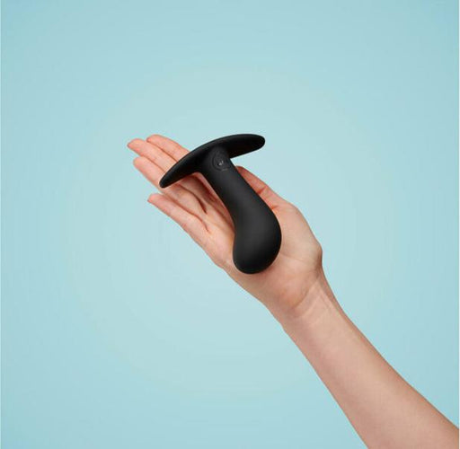 A hand holding a Fun Factory Bootie Large Silicone Anal & Prostate Plug - Black against a light blue background. The toy, designed for prostate play, has a tapered end and a wide base. The hand is presented palm up and centered within the image frame.