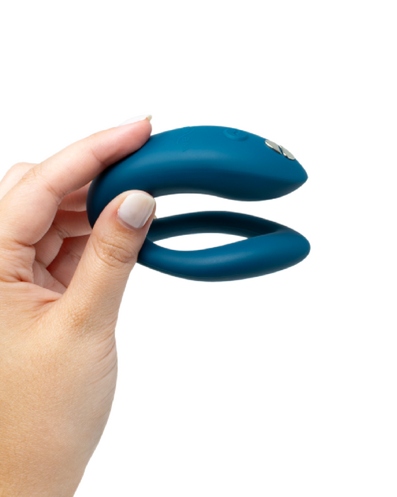 A hand holding a We-Vibe Sync O Hands-Free Wearable Couples Vibrator - Green with a button, isolated on a white background.