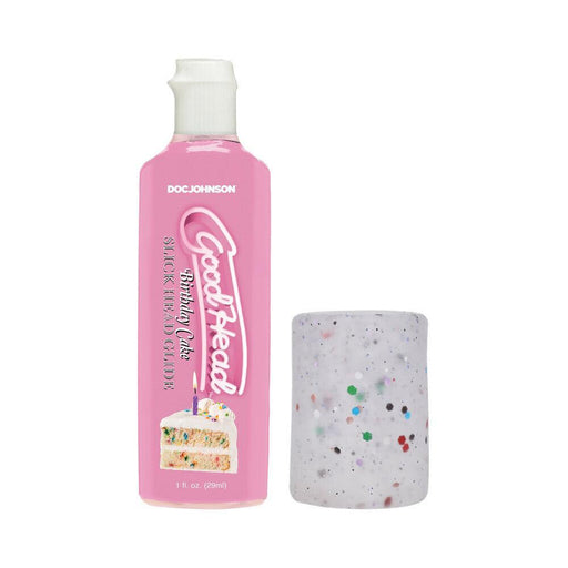 A pink bottle labeled "Birthday Cake Slick Head Glide" is positioned beside a speckled cylindrical container from the GoodHead Birthday Blowjob Kit by Doc Johnson. The bottle displays an image of a cake slice on its front.
