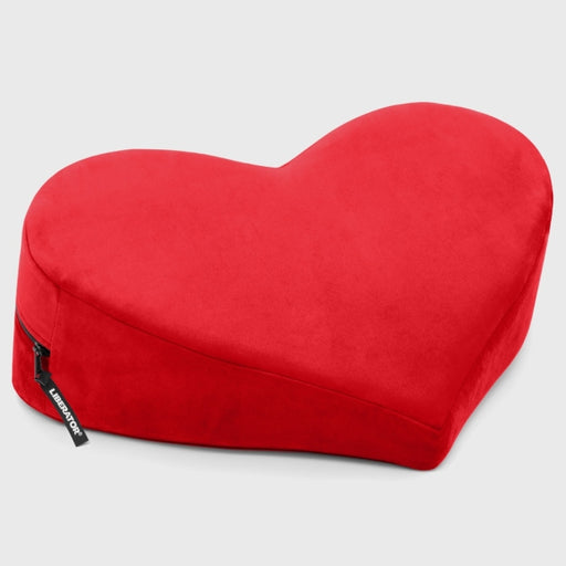 The Liberator Heart Wedge Sex Positioning Cushion, a plush red heart-shaped pillow with a black zipper and tag, rests on a light gray background—ideal for stylish sex furniture or as a playful G-spot pillow.