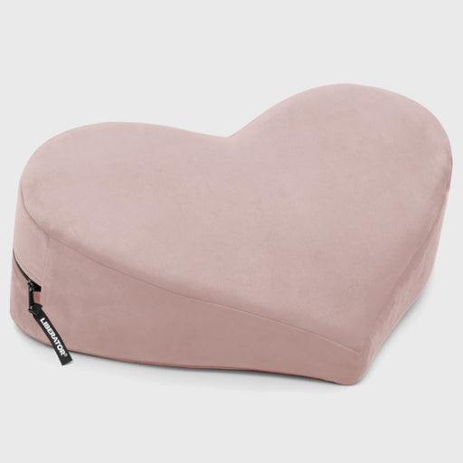 The Liberator Heart Wedge Sex Positioning Cushion is a soft, light pink, heart-shaped pillow with a side zipper, shown lying on a plain light background.