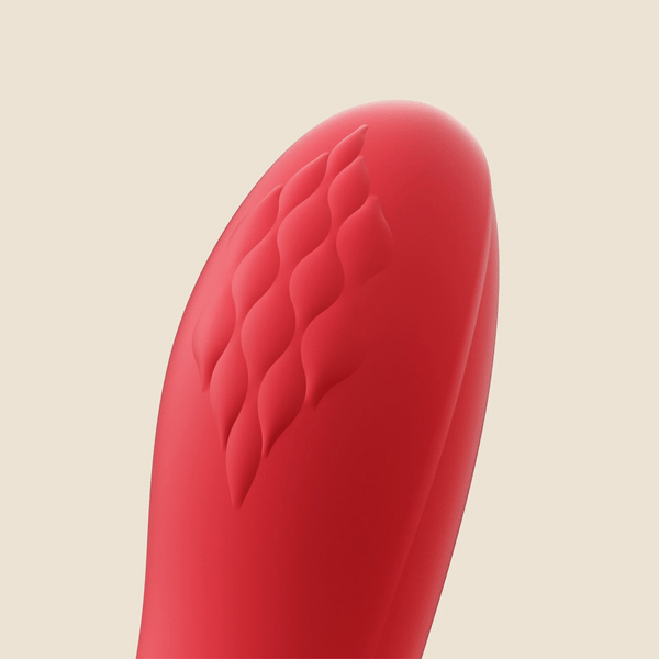 Close-up of the tip of the Fortexa Kinky Finger Rabbit Vibrator with App Control, featuring red silicone and a diamond-textured pattern, shown on a smooth surface against a light beige background.
