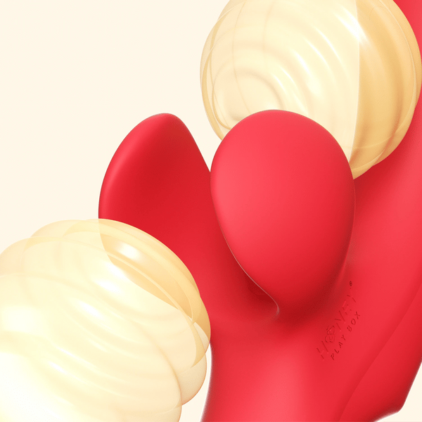 Close-up of the bright red Fortexa Kinky Finger Rabbit Vibrator with app control, featuring two soft yellow spiral-textured attachments for enhanced clitoral stimulation against a light beige background, with "HEXANE" faintly visible on its surface.