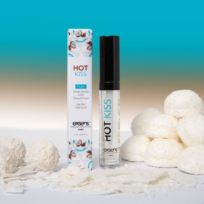 A tube and box of Hot Kiss Arousal Lip Gloss - Coconut 7ml are surrounded by white coconut candies and coconut flakes, set against a gradient blue and beige background.