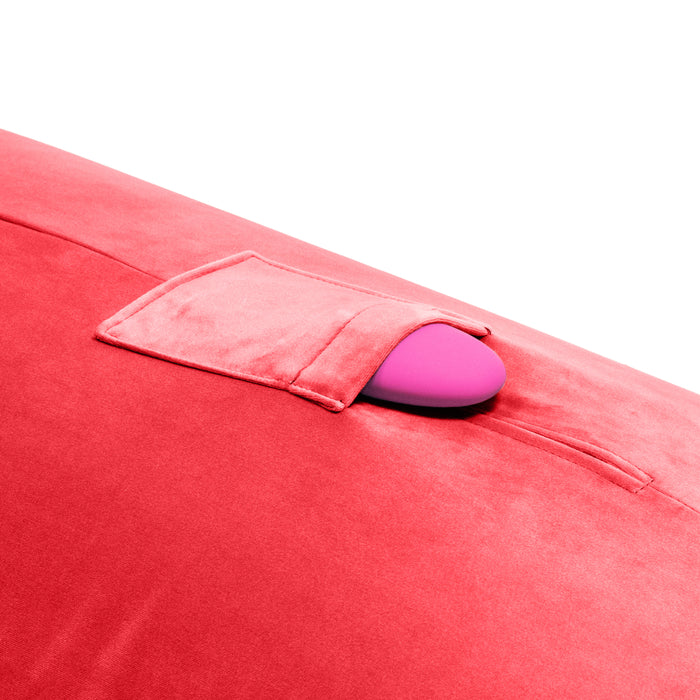 A close-up of the Liberator Humphrey Pillow-Style Sex Toy Mount in bright pink with a small pocket, partially holding a pink oval object, set against a white background.