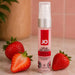 A 1 oz bottle of JO Oral Delight Strawberry Arousal Gel rests on marble beside fresh strawberries. The pink and white bottle features the Strawberry Sensation flavor, highlighting delicious oral pleasure against a softly blurred background.