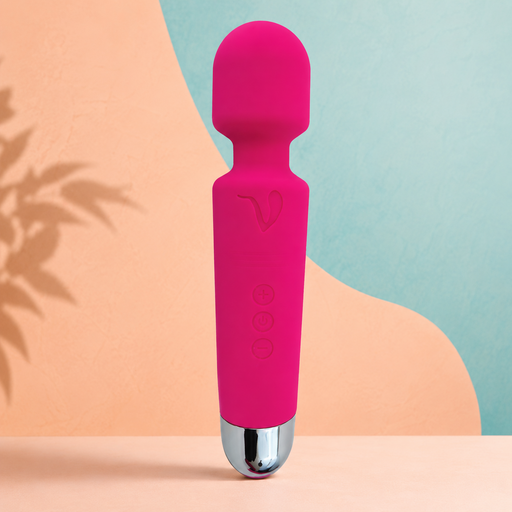 The Mini Halo Extra Powerful Wand Vibrator in bright pink, featuring a rounded top and silver base, stands upright on a peach surface with a pastel blue and peach abstract background.