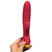 A hand with red-painted nails holds the WOW Jazz Beginner's Silicone Rabbit Vibrator, featuring a pink and yellow design, against a white background. This vibrator, designed for G-spot stimulation, boasts a smooth, elongated shape with a smaller attachment on the side.