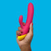 A hand with painted red nails holds a pink and yellow Jazz Beginner's Silicone Rabbit Vibrator by WOW against a bright blue background.