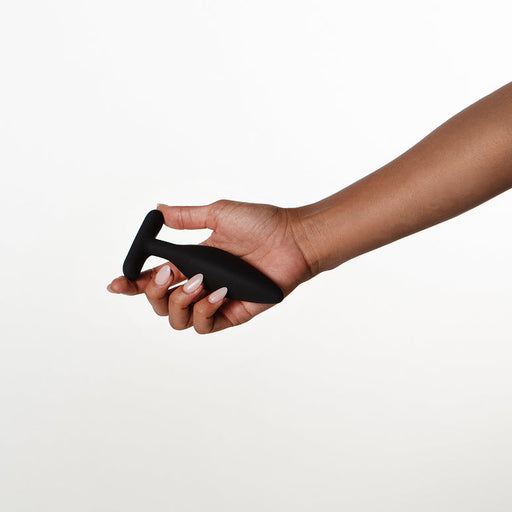 A hand holds the Je Joue Egon Powerful Remote Control Vibrating Butt Plug, a black silicone plug with a T-shaped base, against a plain white background.