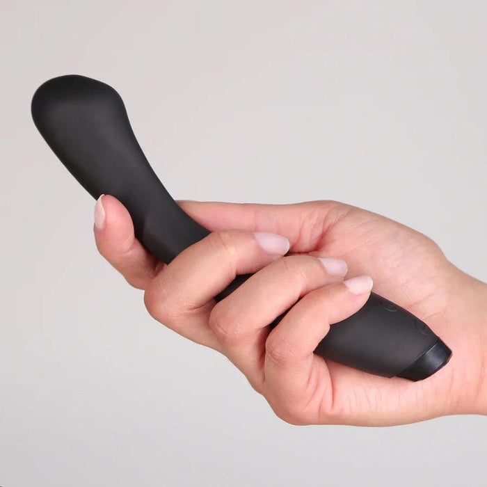 A hand holds the Je Joue Juno Flex G Spot Vibrator - Black, a sleek and sophisticated device with a curved design and rounded tip, showcased against a neutral background. The vibrator is approximately the length of the hand and features a smooth, matte finish from the renowned brand Je Joue.