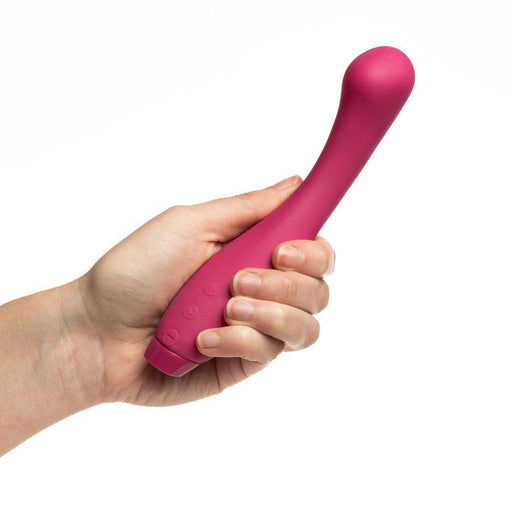A hand holding a Je Joue Juno G Spot Vibrator - Fuchsia by Je Joue, known for its rumbly vibrations, against a white background. The vibrator has a smooth surface with button controls near the base.