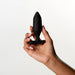 A manicured hand holds the Je Joue Onyx Large Powerful Remote Control Vibrating Butt Plug, a sleek black silicone toy known for its deep rumbly vibrations, against a plain white background.
