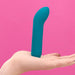 The Je Joue Powerful Internal or External Bullet in teal, a premium silicone vibrator with a sleek and smooth waterproof design, is balanced upright on a person's open palm against a solid pink background.