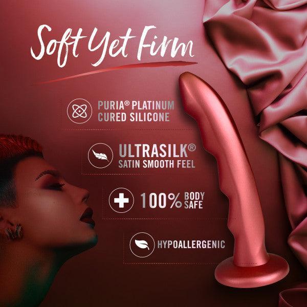 The Jealousy 7 Inch Rippled Silicone Dildo by Blush is elegantly displayed on silky, red fabric. The accompanying text highlights its features: "Soft Yet Firm," "Made with Puria™ Platinum Cured Silicone," "Ultrasilk® Satin Smooth Feel," "100% Body Safe," and "Hypoallergenic." Ideal for g-spot stimulation, a woman's face is partially visible to the left.