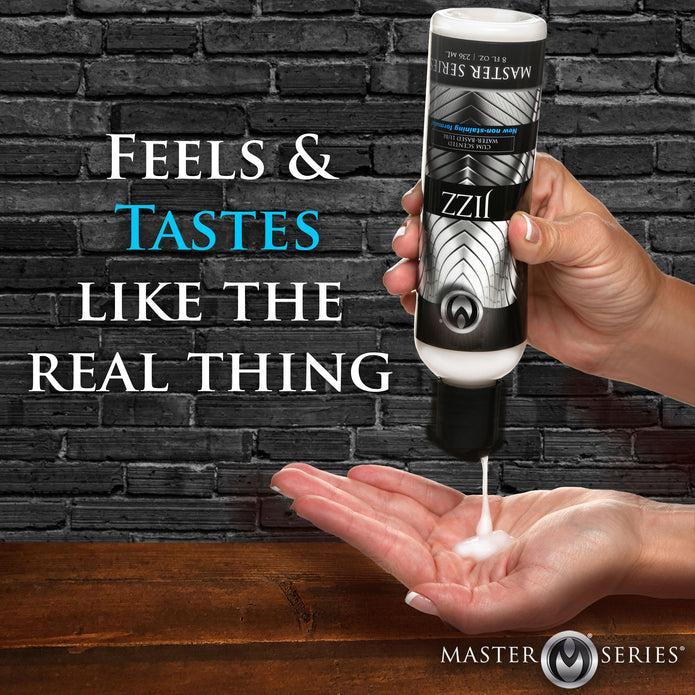 A person is dispensing a white liquid lube from a bottle labeled "XR Brands Jizz Ultra Realistic Cum Scented Lube 8.5oz" into their hand. The background features a dark brick wall with text that reads, "Feels & Tastes Like The Real Thing." The bottom of the image shows a wooden surface.