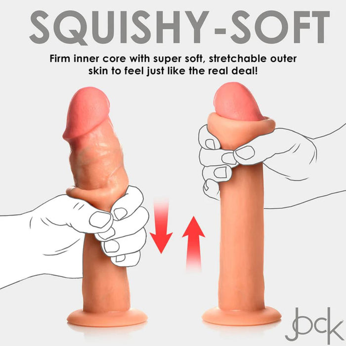 Two hands squeezing the Jock Real Skin 8.5 Inch Silicone Suction Cup Dildo in vanilla, highlighting its dual density design with a firm inner core and super soft, stretchable outer skin. The text above reads "SQUISHY-SOFT." Red arrows indicate the squeezing motion, while the "bck" logo is displayed at the bottom. The product is offered by XR Brands.