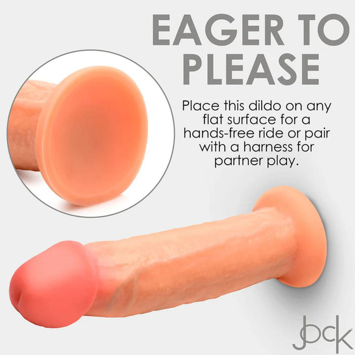 Close-up image of the Jock Real Skin 8.5 Inch Silicone Suction Cup Dildo by XR Brands, featuring a dual-density design. Text reads: "Eager to Please. Place this vanilla-toned dildo on any flat surface for a hands-free ride or pair with a harness for partner play." Dildo is light skin-toned with pinkish tip.