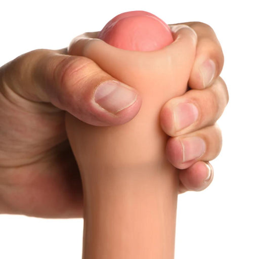 A hand holds the XR Brands Jock Real Skin 8.5 Inch Silicone Suction Cup Dildo in a vanilla color, which features a dual-density design with a beige, flesh-like material and a rounded pink end, reminiscent of a toy or stress ball.