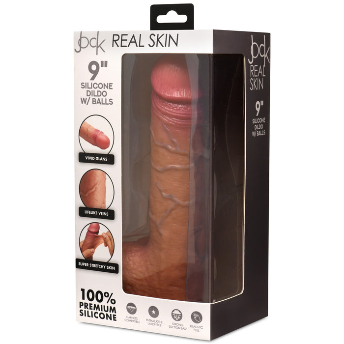 The image shows the Jock Real Skin 9 Inch Silicone Suction Cup Dildo with Balls in a caramel color, designed by XR Brands. The packaging emphasizes features such as "vivid glans," "lifelike veins," and "super stretchy skin," along with labels like "Real Skin" and "100% Premium Silicone.