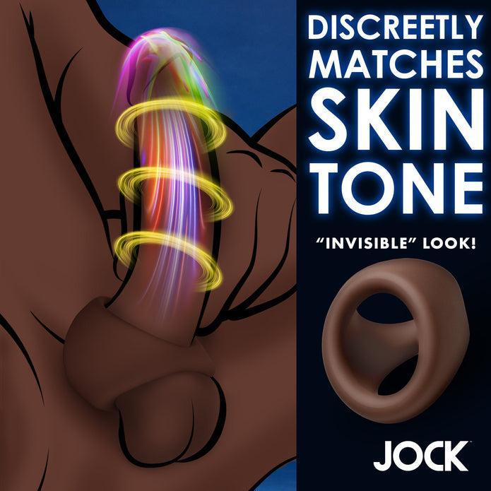 Illustration of a brown penis wearing the JOCK Silicone Cock & Ball Ring in Dark Skin Tone, with colorful vibration lines. Text reads "Discreetly matches skin tone," "'invisible' look!" and "Jock" along with an image of the ring product.