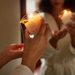 A person pours warm melted wax from the Melt Together Massage Oil Candle by Dame (Green Tea, Fig & Cedarwood) onto their hand, while another in a white robe stands behind them holding a similar candle.
