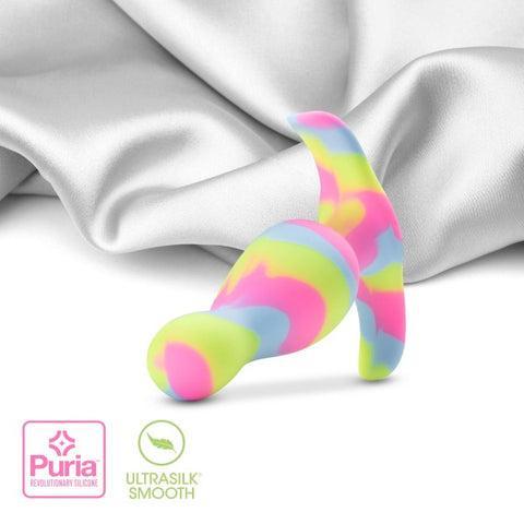 A vibrant Kaleido Silicone Beginner's Butt Plug by Blush, featuring a swirled pattern of pink, yellow, blue, and green, rests on a smooth, white fabric. Designed for anal beginners, this toy has a curved, ergonomic design. Logos indicating "Puria Revolutionary Platinum-Cured Silicone" and "Ultrasilk Smooth" are displayed in the lower left corner.