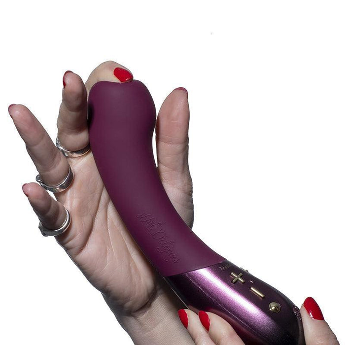 A hand with red nails and multiple rings is holding a burgundy, curved G-spot vibrator with control buttons and the text "Hot Octopuss" embossed on it. The product, named Kurve Dual Motor G-Spot Vibrator by Hot Octopuss, is set against a white background.