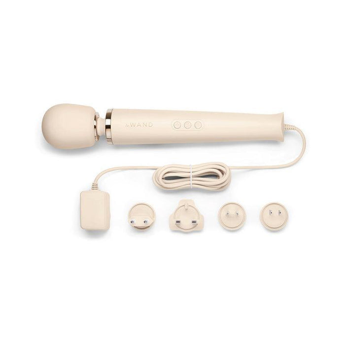 The Le Wand Plug In Powerful Wand Vibrator in cream, by Le Wand, is a beige handheld massager with a rounded head and an attached cord that leads to a power adapter. The set includes the vibrator, a coiled cord, a zippered storage case, and four interchangeable plug attachments. It boasts three control buttons on its body for ease of use.