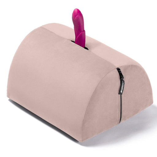The Liberator BonBon Rideable Sex Toy Mount is a light pink, wedge-shaped foam pillow with a built-in slot for holding an upright vibrator and a black side zipper, offering discreet, hands-free pleasure.