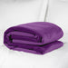 The Liberator Fascinator Throw King Size Waterproof Sex Blanket, in purple, adds style and a moisture barrier to your white bed while blending seamlessly with white pillows in the background.