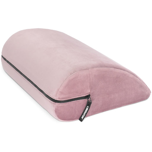 The Liberator Jaz Motion is a pink, velvet-like, half-moon shaped cushion with a zippered side and "Kensington" tag—ideal for bedroom support or as a versatile alternative to traditional positioning pillows.