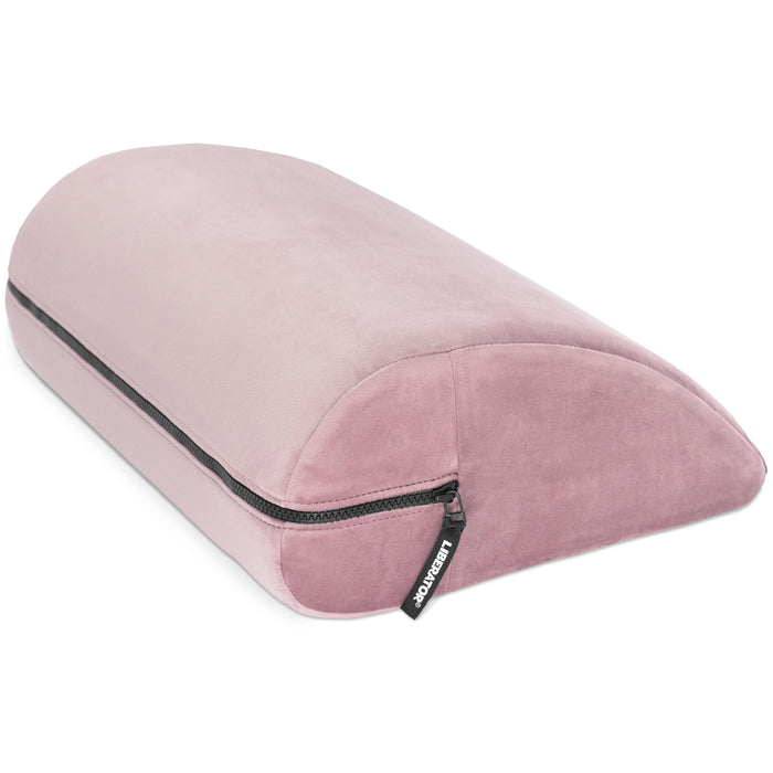 The Liberator Jaz Motion is a pink, velvet-like, half-moon shaped cushion with a zippered side and "Kensington" tag—ideal for bedroom support or as a versatile alternative to traditional positioning pillows.