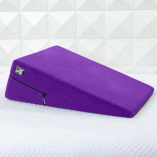 A Liberator Ramp Sex Positioning Cushion - 30 Inches in purple with a zippered cover rests on a white textured surface before a geometric tiled wall.