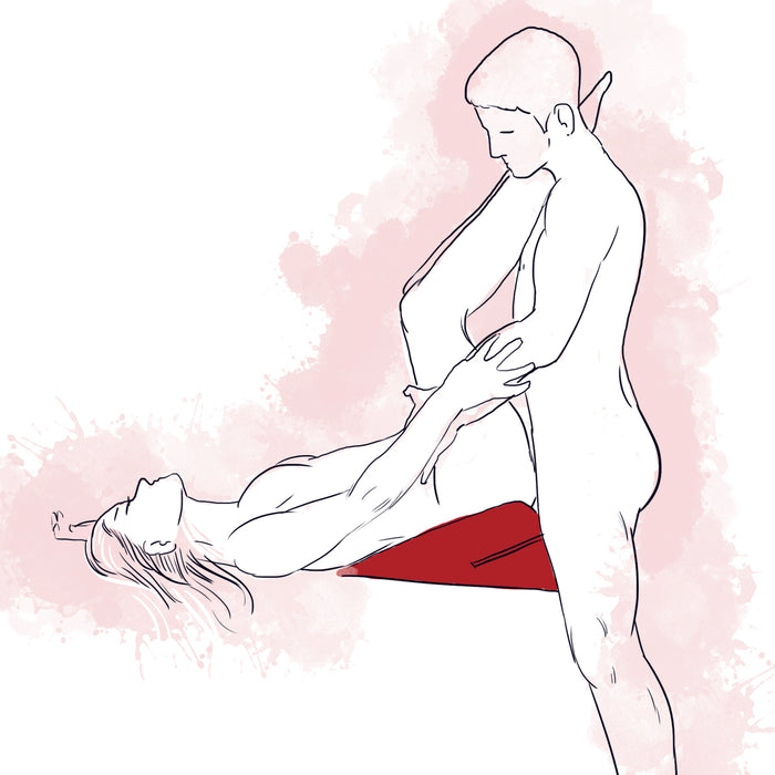 A stylized drawing shows two nude people having sex using the Liberator Wedge Sex Positioning Cushion - 30 Inches. One partner lies on the wedge, legs raised, while the other stands holding their legs. Soft pink watercolor splashes fill the background.
