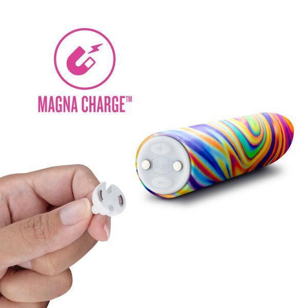 A hand holding a small, circular magnetic charger next to a colorful, tie-dye patterned cylindrical device. The text "MAGNA CHARGE™" with a magnet icon is displayed to the left of the Limited Addiction Power Bullet Vibe - Psyche from Blush, featuring 10 deep rumbly vibrations.