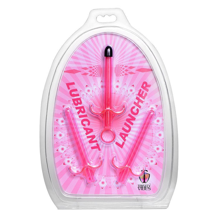 The image showcases a plastic package containing a set of three pink Lubricant Launcher 3-Pack Pink by XR Brands, ideal for both vaginal moisturizing and anal play. The background is pink with white patterns, and the words "Lubricant Launcher" are written in bold.