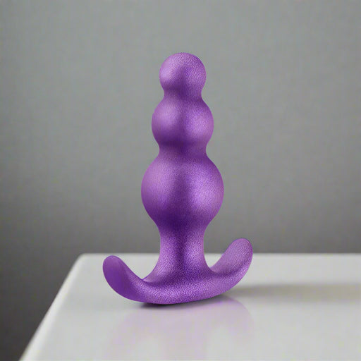 Introducing the Matrix Beginner Soft Silicone Textured Butt Plug by Blush in Galactic Purple. This platinum cured silicone beaded butt plug features three rounded beads that gradually increase in size from top to bottom, complemented by a curved, flared base that ensures safe insertion and removal. Perfect for extended wear, its surface boasts a subtle shimmer finish.