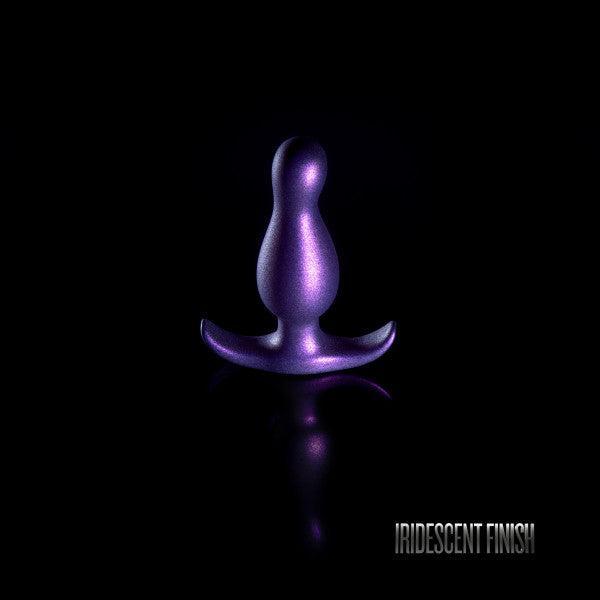 A small, iridescent purple Matrix First Time Flexible Silicone Butt Plug - Galactic Purple by Blush, featuring a bulbous top and flared base, stands upright on a black background. Text in the lower right corner reads "IRIDESCENT FINISH.