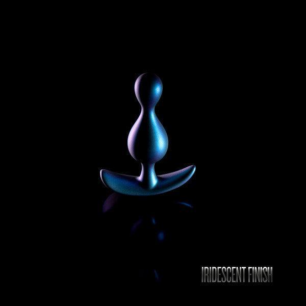 A sleek, bulbous Matrix First Time Soft Silicone Butt Plug - Shimmery Green by Blush, with a metallic iridescent finish made from platinum-cured silicone, is displayed against a dark background. The text "IRIDESCENT FINISH" appears in the bottom right corner.