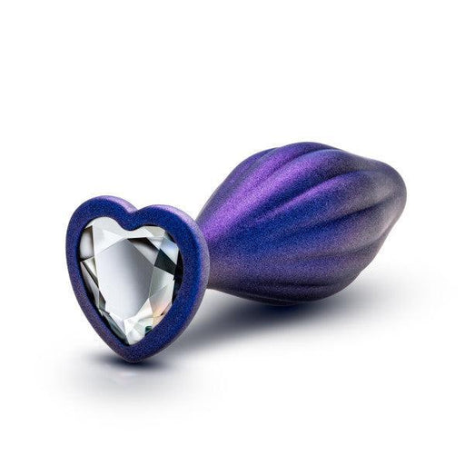 The Matrix Wavy Bling Plug with Sparkly Heart Base by Blush is a purple, seashell-shaped beginner plug with a heart-shaped base. The base features a sparkling, clear crystal embedded in the center. It has a smooth, glossy finish and a gradient texture that transitions from dark purple to a lighter shade.