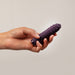 A hand holds a textured, dark purple vibrator from the Midnight Magic Couples' Sex Toy Gift Set, displayed against a plain light background.