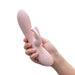 A hand holding the Blush Morgan Beginner G-Spot Rabbit Vibrator, showcasing its smooth pink silicone texture and elegantly curved design. The device features an insertable shaft along with an external clitoral stimulator shaped like rabbit ears, ideal for clitoral stimulation. Control buttons are conveniently located on the handle. The background is plain white.