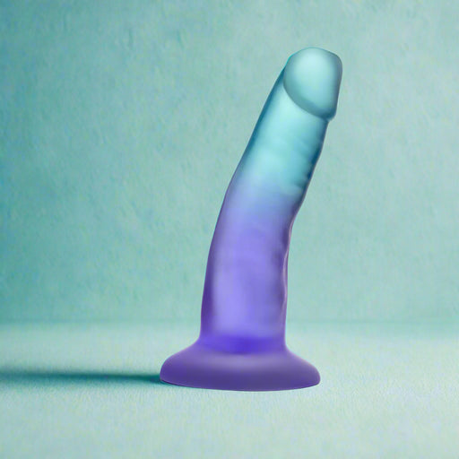 The Morning Dew Small 5 Inch Dildo with Suction Cup - Blue, a translucent gradient blue and purple dildo with a flared base, stands upright on a light teal surface. It's beginner-friendly, suction-based, and harness compatible for versatile play.